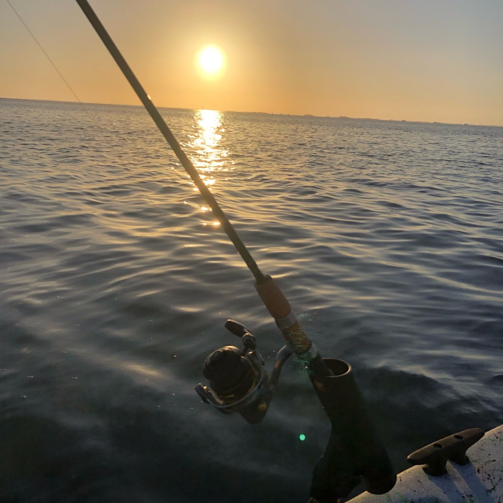 Fishing rod in a rod holder on the boat with the sun rising over the water in the background