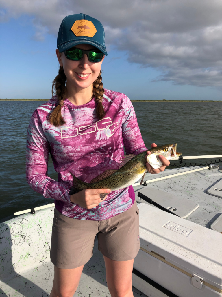 girl holding a trout on a boat in shorts and a hat